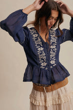 Load image into Gallery viewer, Woman wearing a blue embroidered blouse with a beige background