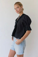 Load image into Gallery viewer, Woman wearing a black blouse with ruffled sleeves and light blue denim shorts against a white background