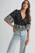 Load image into Gallery viewer, Woman wearing a black top with white lace details and light blue jeans on a white background