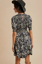 Load image into Gallery viewer, Woman wearing a floral dress and black hat against a beige background