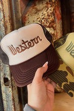 Load image into Gallery viewer, Two 'Western' branded hats, one brown and one with a camouflage pattern, held by a hand against a rustic background.