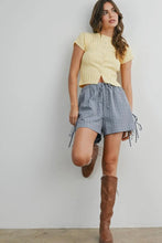 Load image into Gallery viewer, Woman wearing a yellow top, plaid shorts, and brown knee-high boots against a plain background