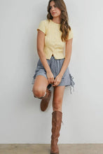 Load image into Gallery viewer, Woman wearing a yellow top and plaid skirt with brown knee-high boots against a white wall.