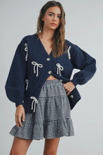 Load image into Gallery viewer, Woman wearing a navy cardigan with white bow details and a plaid skirt on a gray background