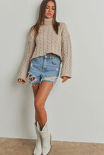 Load image into Gallery viewer, Woman wearing a beige cable knit sweater, denim shorts, and white boots on a plain background