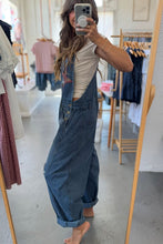 Load image into Gallery viewer, Person wearing blue denim overalls taking a mirror selfie in a clothing store.