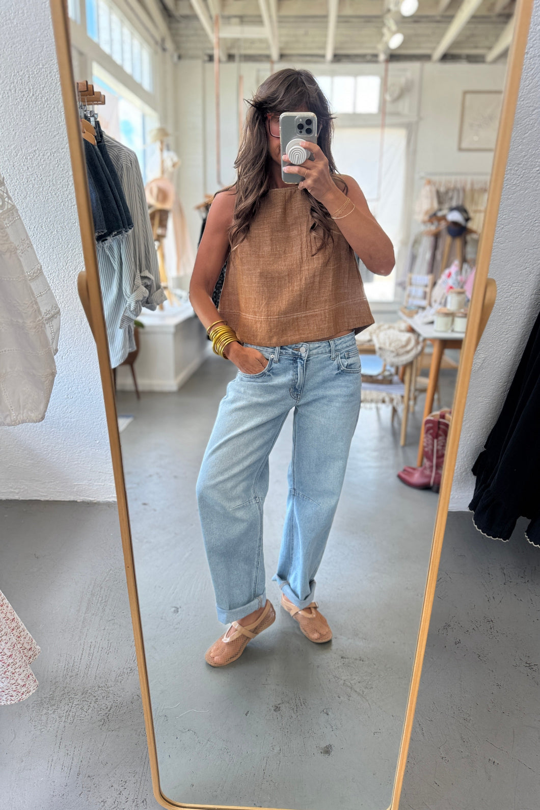 Person taking a mirror selfie wearing a brown top and light blue jeans in a store.