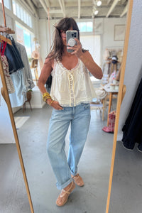 Woman taking a mirror selfie wearing a white lace top and light blue jeans in a store.