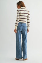 Load image into Gallery viewer, A woman is shown from behind wearing a cream and brown striped long-sleeve top and high-waisted, wide-leg blue denim jeans with diagonal seam details down the front of the legs, paired with brown heels, against a light gray studio background.
