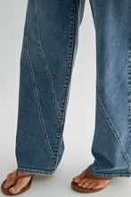 Load image into Gallery viewer, Close-up of a person's legs wearing wide-leg blue denim jeans and brown flat sandals against a light gray studio background.