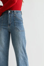 Load image into Gallery viewer, Close-up of a person wearing light blue wide-leg denim jeans with a red long-sleeve top, shown against a plain light gray studio background.