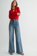 Load image into Gallery viewer, A woman modeling a red long-sleeve knit top with a keyhole cutout and high-waisted, wide-leg blue denim jeans against a light gray studio background.
