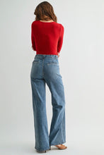 Load image into Gallery viewer, A woman shown from the back wearing a bright red long-sleeve top and light-wash blue wide-leg jeans, standing against a plain light gray studio background.