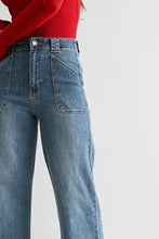 Load image into Gallery viewer, Close-up of a person wearing light blue wide-leg denim jeans and a red long-sleeve top against a plain light gray studio background.