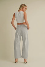 Load image into Gallery viewer, Woman wearing a white sleeveless top and light gray pants on a beige background