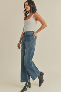 Woman wearing a light gray tank top and blue jeans on a beige background