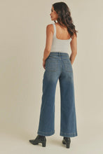 Load image into Gallery viewer, Woman wearing blue jeans and a white tank top on a beige background