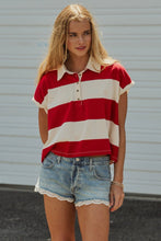 Load image into Gallery viewer, A woman wearing a red and off-white striped short-sleeve polo shirt with light-wash denim shorts, standing in front of a white corrugated metal wall.