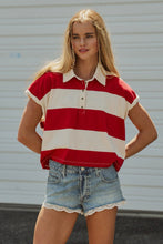 Load image into Gallery viewer, A woman modeling a red and off-white horizontally striped short-sleeve polo shirt with denim shorts, standing in front of a white corrugated metal wall.