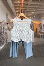 Load image into Gallery viewer, Floral-patterned vest and light blue pants on a hanger in a store setting.