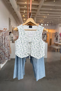 Floral-patterned vest and light blue pants on a hanger in a store setting.