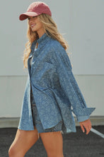 Load image into Gallery viewer, A woman wearing a loose, oversized blue denim shirt with a subtle tonal pattern, paired with denim shorts and a dusty pink baseball cap, walking outdoors against a light gray wall.