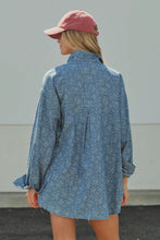 Load image into Gallery viewer, A woman shown from behind wearing a loose, oversized blue denim shirt with a subtle white floral print, paired with a dusty pink baseball cap.