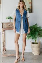 Load image into Gallery viewer, Woman wearing a denim vest over a white dress in a room with a plant and wooden side table.