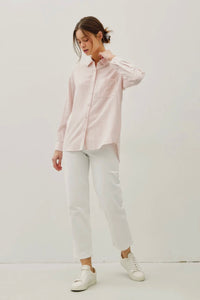 Woman wearing a light pink shirt and white pants on a plain background