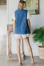 Load image into Gallery viewer, Woman wearing a blue denim vest over a white shirt and shorts in a room with a plant and wooden side table.