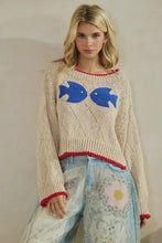 Load image into Gallery viewer, Woman wearing a cream sweater with blue fish designs and denim jeans against a plain background