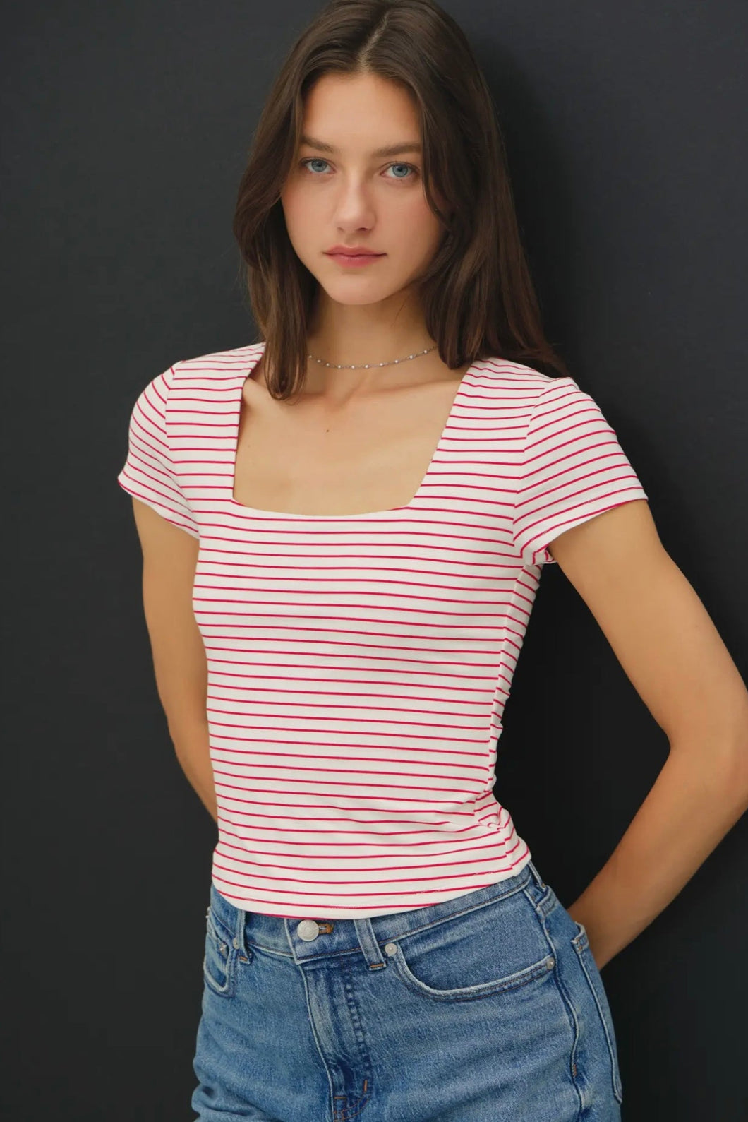 Woman wearing a red and white striped shirt and blue jeans against a black background