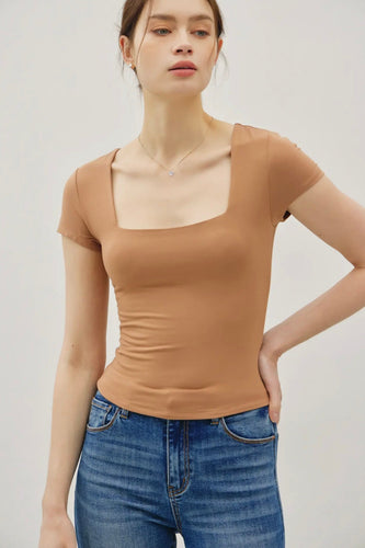 Woman wearing a brown top and blue jeans against a plain background