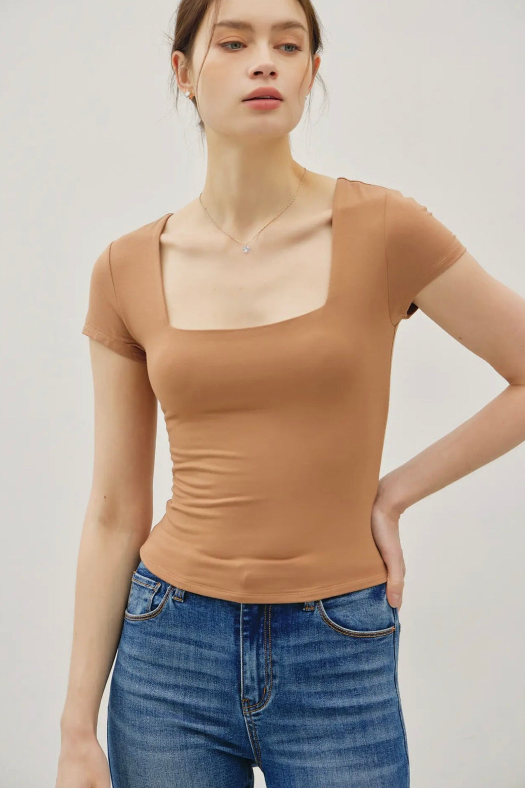 Woman wearing a brown top and blue jeans against a plain background