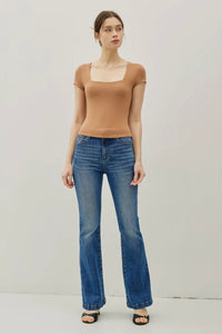 Woman wearing a brown top and blue jeans on a plain background