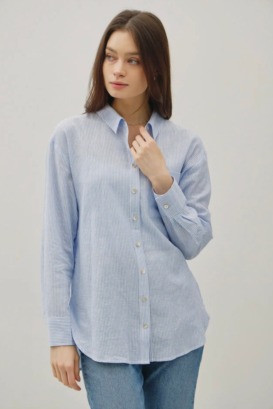 Woman wearing a light blue striped shirt and jeans on a plain background