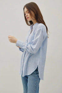 Woman wearing a light blue striped shirt and jeans against a plain background