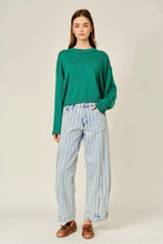 Load image into Gallery viewer, A woman modeling a green long-sleeve knit sweater and light blue vertically striped wide-leg jeans, paired with brown leather loafers, against a plain light beige studio background.