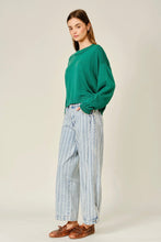 Load image into Gallery viewer, A woman modeling a green long-sleeve knit sweater and light blue vertically striped wide-leg jeans with brown leather loafers, standing against a plain light beige studio background.