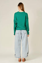Load image into Gallery viewer, A woman viewed from behind wearing a green long-sleeve sweater, wide-leg light blue and white striped pants, and brown flat shoes against a plain light beige studio background.