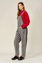 Load image into Gallery viewer, A woman modeling a pair of gray overall-style pants with a white polka dot pattern, worn over a red long-sleeve top and paired with black clogs, against a plain light gray studio background.