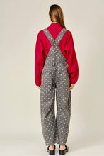 Load image into Gallery viewer, A model shown from the back wearing gray wide-leg denim overalls with a white polka-dot pattern, layered over a red long-sleeve top, against a light beige studio background.