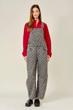 Load image into Gallery viewer, A woman modeling gray wide-leg overall pants with a white polka dot pattern, worn over a red long-sleeve top and black shoes, against a light beige studio background.