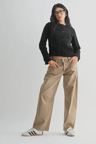 Person wearing a black cropped jacket and beige pants on a white background