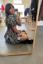 Load image into Gallery viewer, Woman taking a mirror selfie wearing a floral dress in a room with a mirror and furniture.