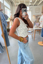 Load image into Gallery viewer, Woman taking a mirror selfie wearing a floral top and light blue jeans in a clothing store.