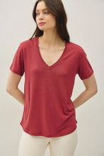 Load image into Gallery viewer, A woman wearing a short-sleeve V-neck t-shirt in heathered red, paired with off-white pants, photographed against a neutral light gray studio background.