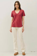 Load image into Gallery viewer, A woman modeling a short-sleeve V-neck t-shirt in a dusty rose red color, paired with off-white trousers and brown shoes, standing against a plain light gray studio background.