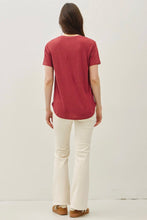 Load image into Gallery viewer, A woman viewed from behind wearing a muted red short-sleeve t-shirt and off-white flared pants, standing against a plain light background.