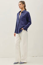 Load image into Gallery viewer, A woman modeling a navy blue long-sleeve button-up shirt with white wide-leg trousers and blue pointed flats, standing against a plain off-white studio background.